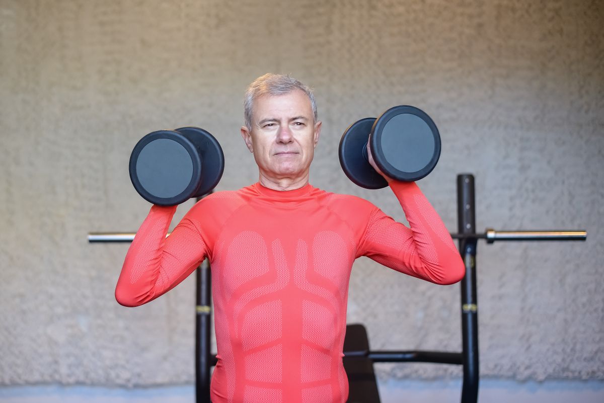 Zreliji muškarac vježba s bučicama u zatvorenom prostoru